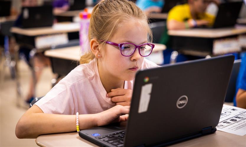A girl wearing a pink shirt and glasses uses a Chromebook